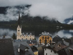 Scenic view of Hallstatt village with iconic church and serene lake surrounded by misty mountains.